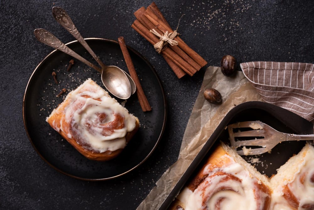 Delicious cinnamon roll cheesecake topped with creamy frosting and cinnamon swirl, served on a white plate