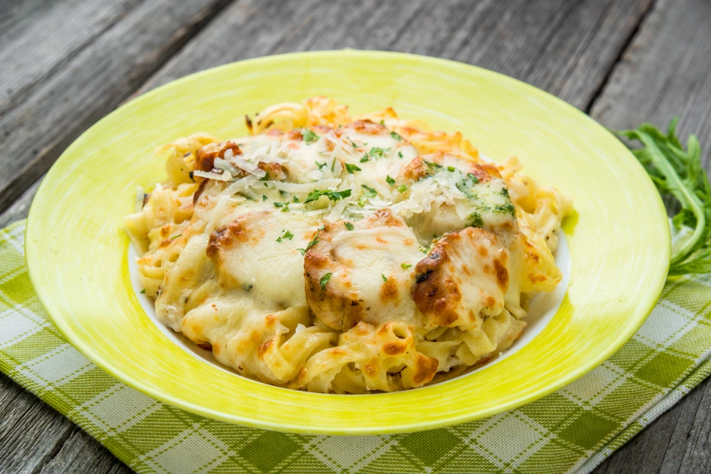 A delicious bowl of French onion pasta with chicken, topped with melted cheese and garnished with fresh herbs.