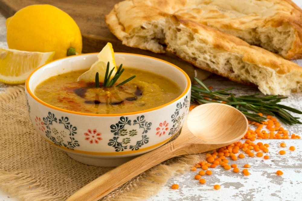 A bowl of Persian lentil soup, garnished with fresh herbs. The soup appears hearty and warm, showcasing its nutritious ingredients and inviting presentation.