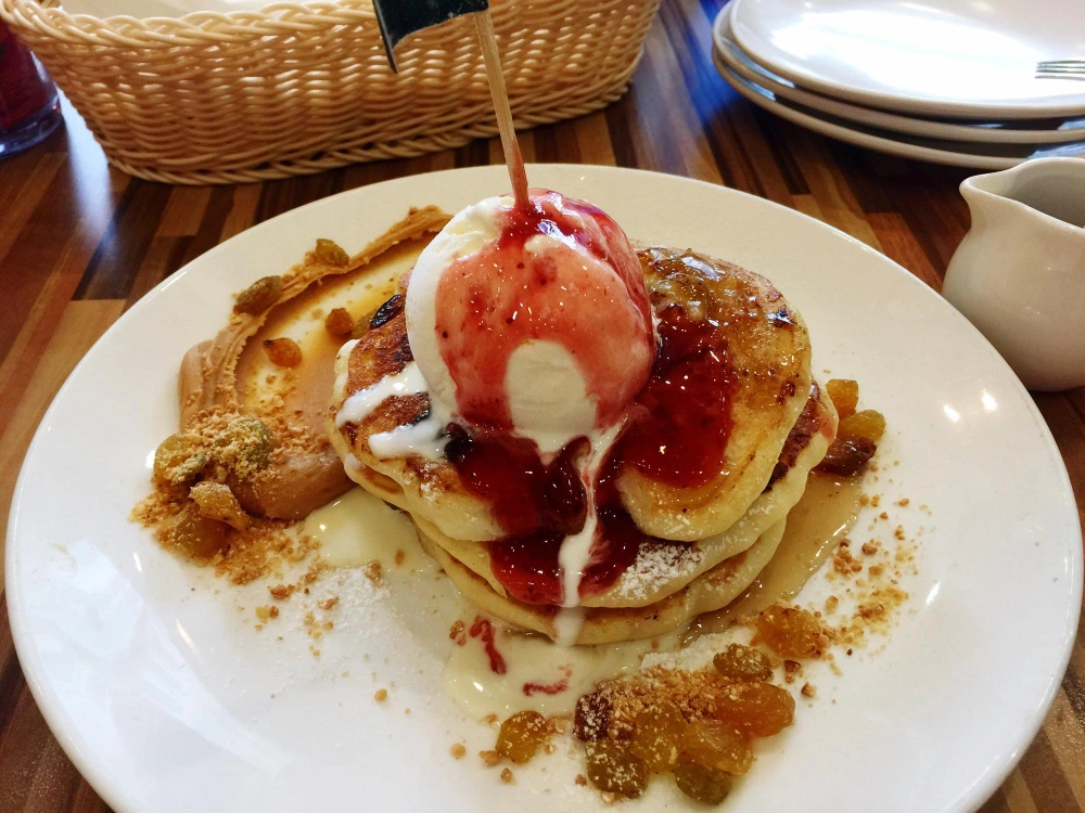 A stack of fluffy coffee pancakes topped with whipped cream and drizzled with maple syrup