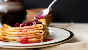 Stack of thin, golden crepes made with pancake mix, served on a white plate with fresh berries and a drizzle of syrup.