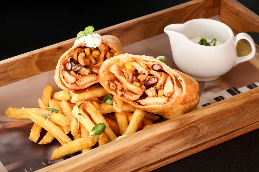 A Hot Honey Chicken Sandwich served with a side of fries and a dipping sauce on a rustic wooden table.