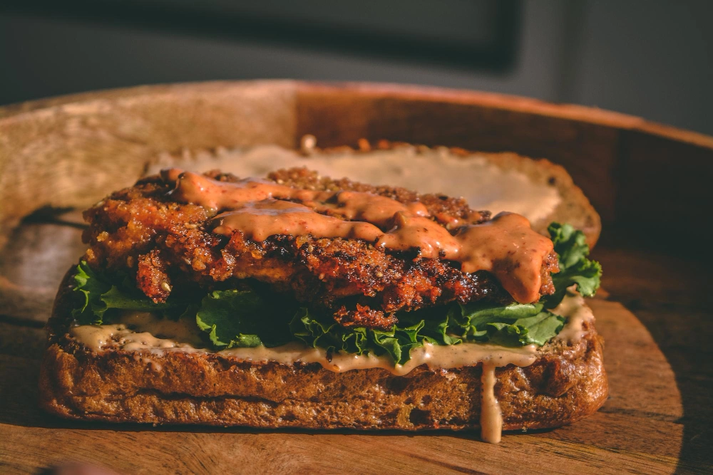 A close-up of a crispy hot honey chicken sandwich with lettuce  on a toasted bun.