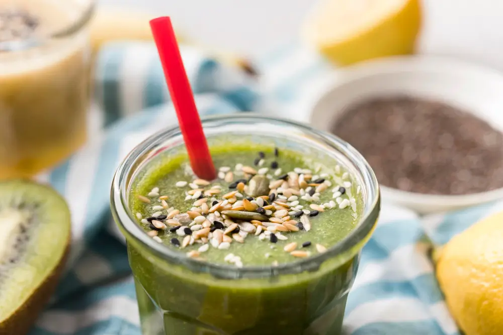 Bee Pollen Smoothie: Discover Its Health Benefits Today! 4 A green bee pollen smoothie in a clear glass, with seeds, placed on a stone table outdoors.