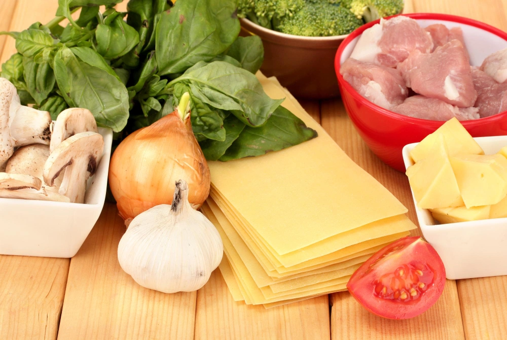  Ingredients laid out for chicken and broccoli lasagna, including lasagna noodles, chicken, broccoli, and mozzarella cheese.