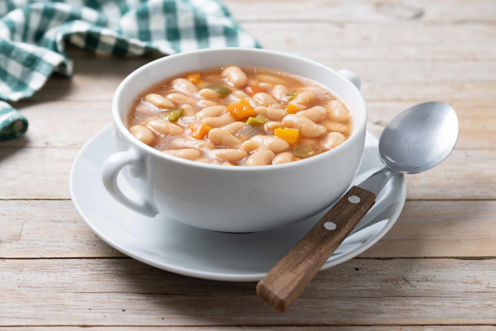 A bowl of lemony white bean soup with turkey and greens, served on a rustic wooden table.