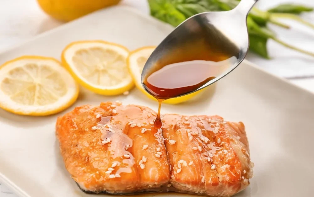 A beautifully plated dish featuring grilled salmon belly, with lemon slices and honey