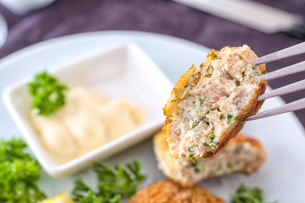 A slice of tuna and salmon loaf served on a plate with a side of mixed greens.